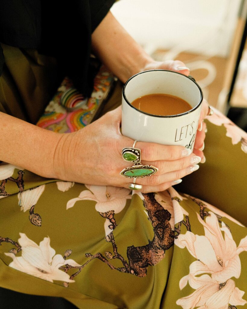 Erin holding her morning coffee with green stone rings on her fingers