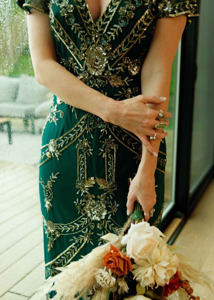 Erins wearing her green dress with gold and silver embroidered design paired with green gemstone rings and her floral bouquet 