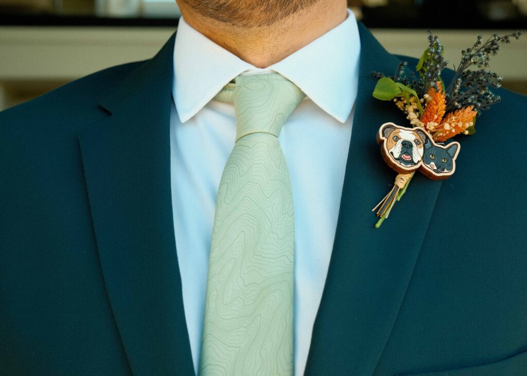 josh's dark teal suit with a white button up, a sage green topographical map tie of Breckinridge and his boutonniere 