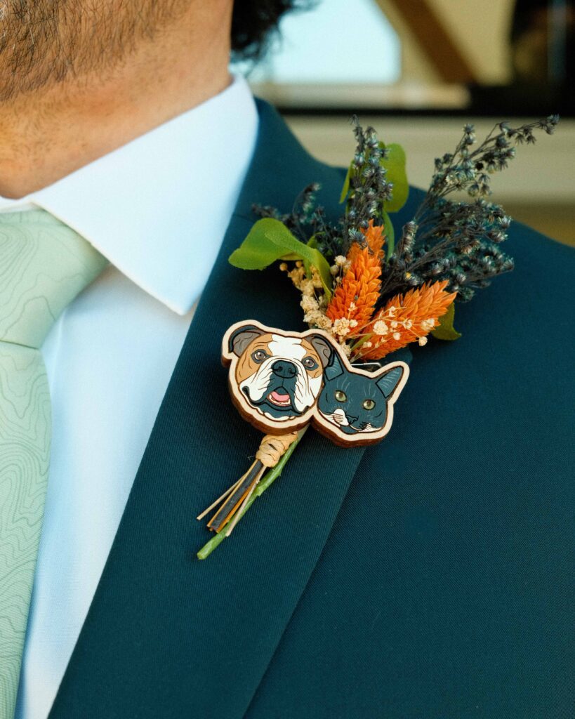 Josh wearing a dark teal suit with a faux floral boutonniere with their dog and cat faces on a pin