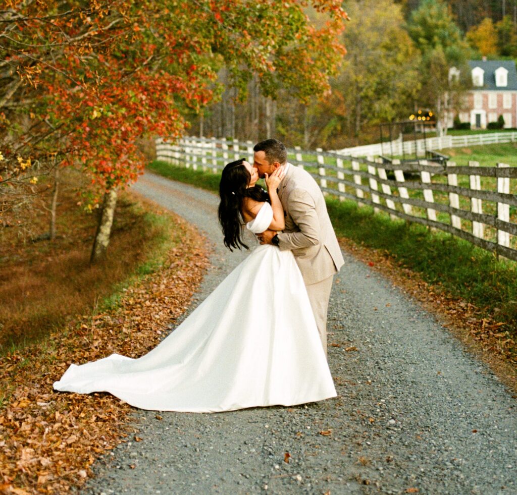 a couple kissing under an autumn drive on a driveway in wedding outfits after a mountainside elopement in North Carolina